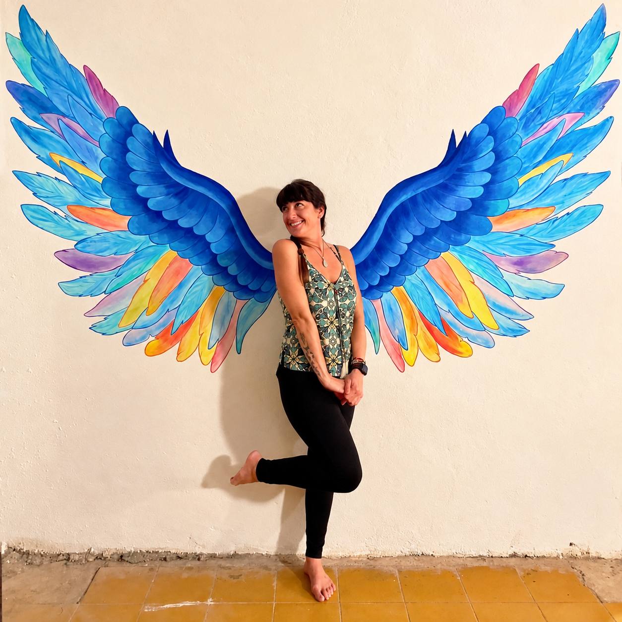 reva-colorful-wings-contact.jpg Reva smiling in front of a colorful painted wings mural.