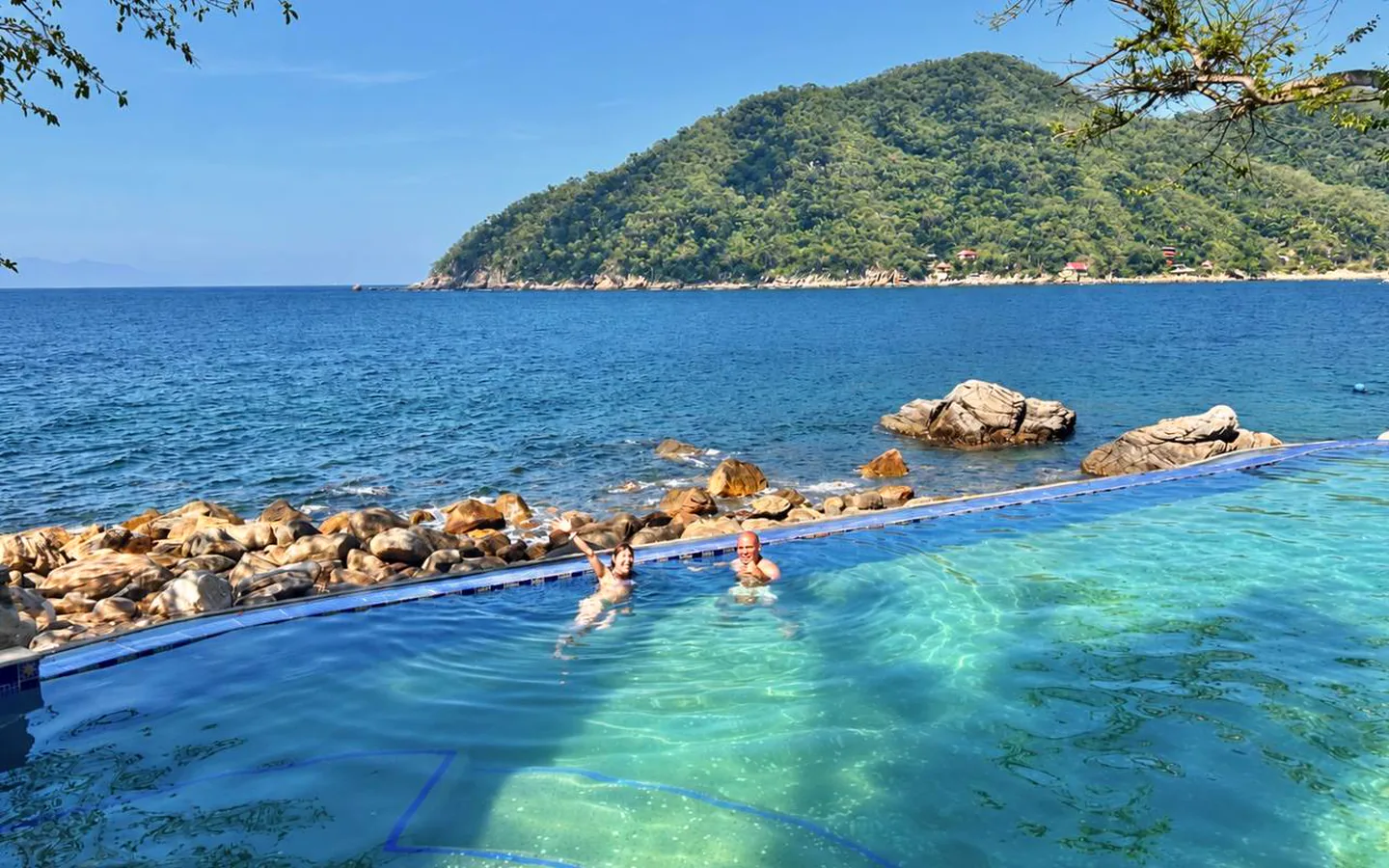 swimming-card-popup-1440x900-perf-v1.webp Two guests swimming in an oceanfront pool overlooking the bay